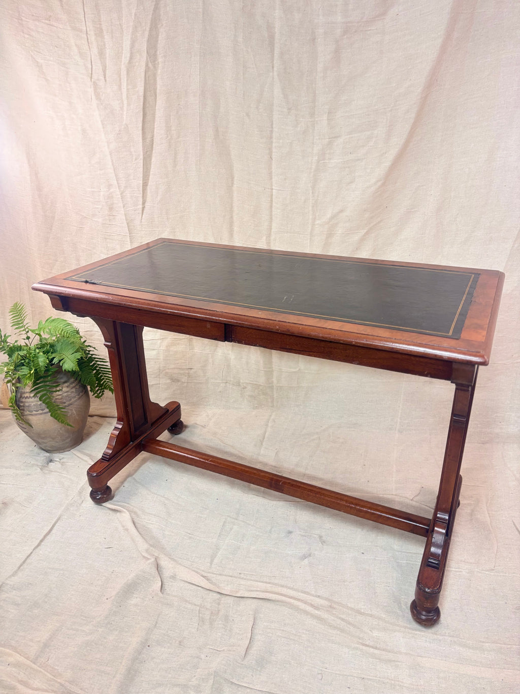 A small wooden table with a leather top against a cream background with a potted plant