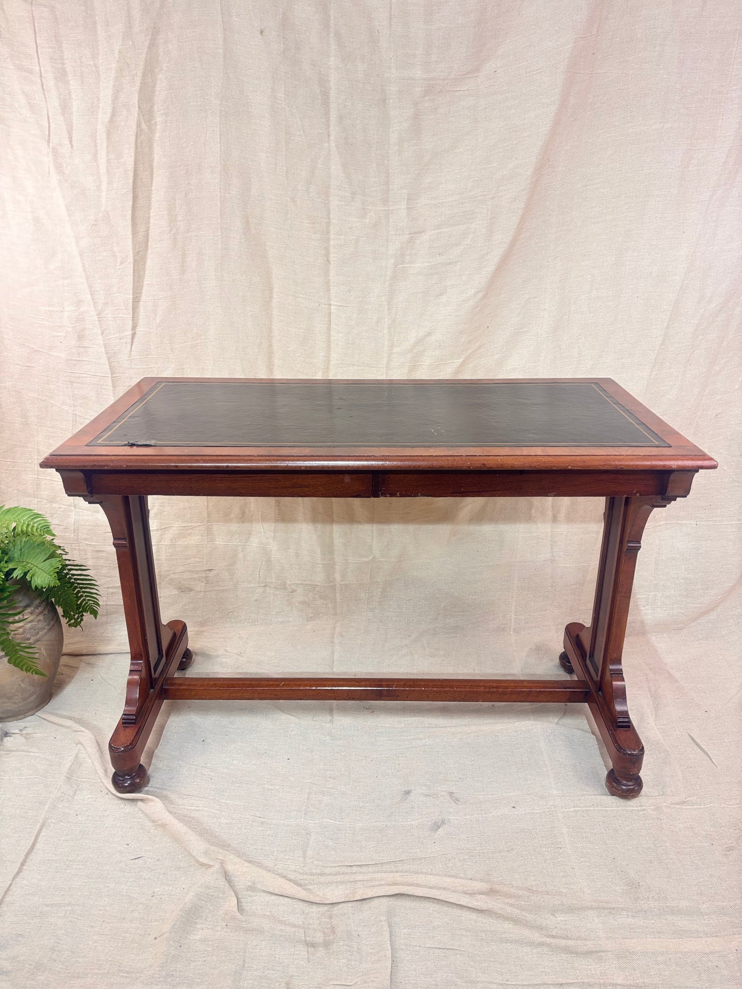 A small wooden table with a leather top against a cream background with a potted plant