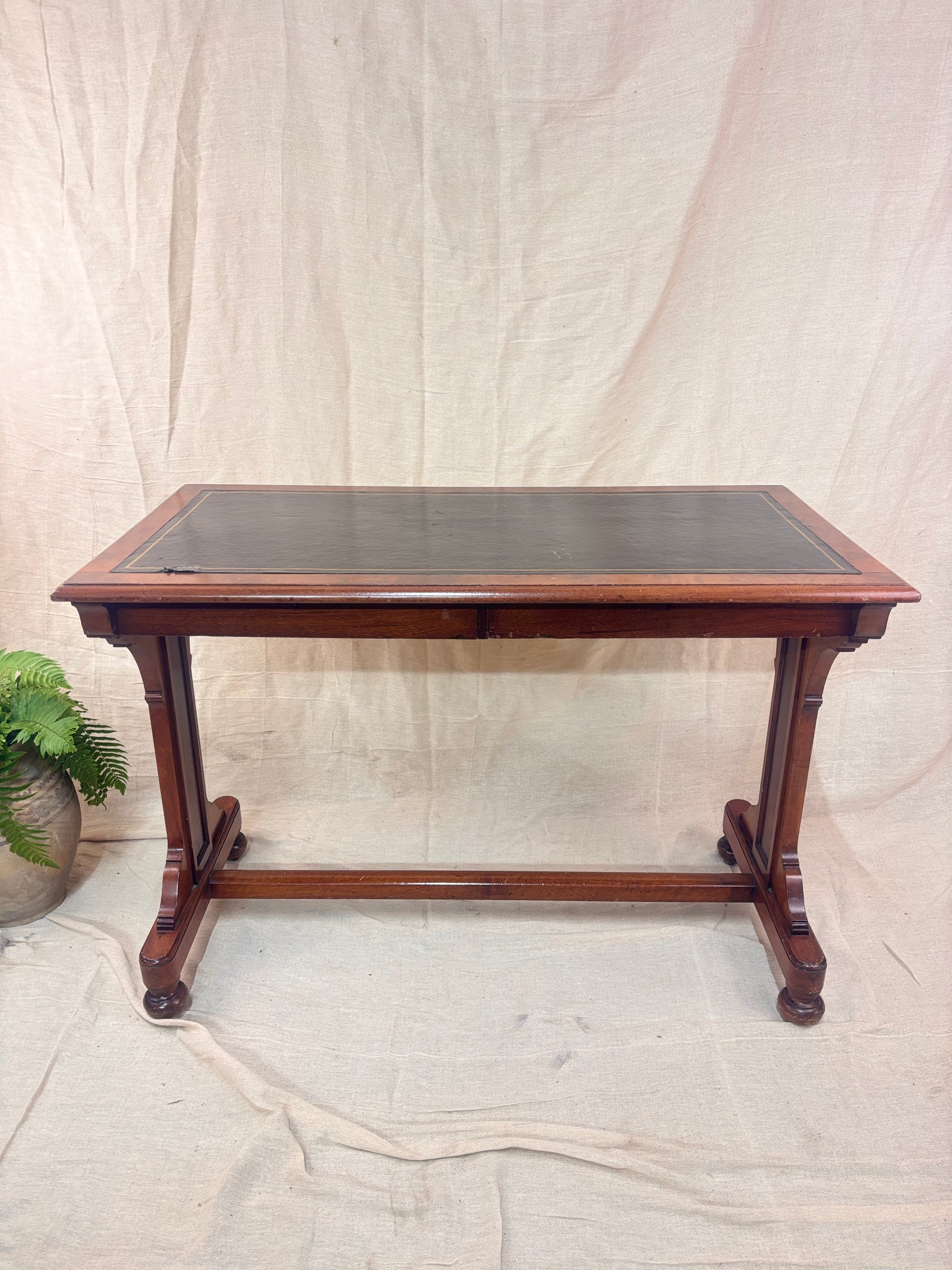 A small wooden table with a leather top against a cream background with a potted plant