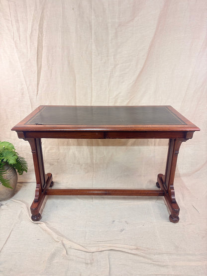 A small wooden table with a leather top against a cream background with a potted plant