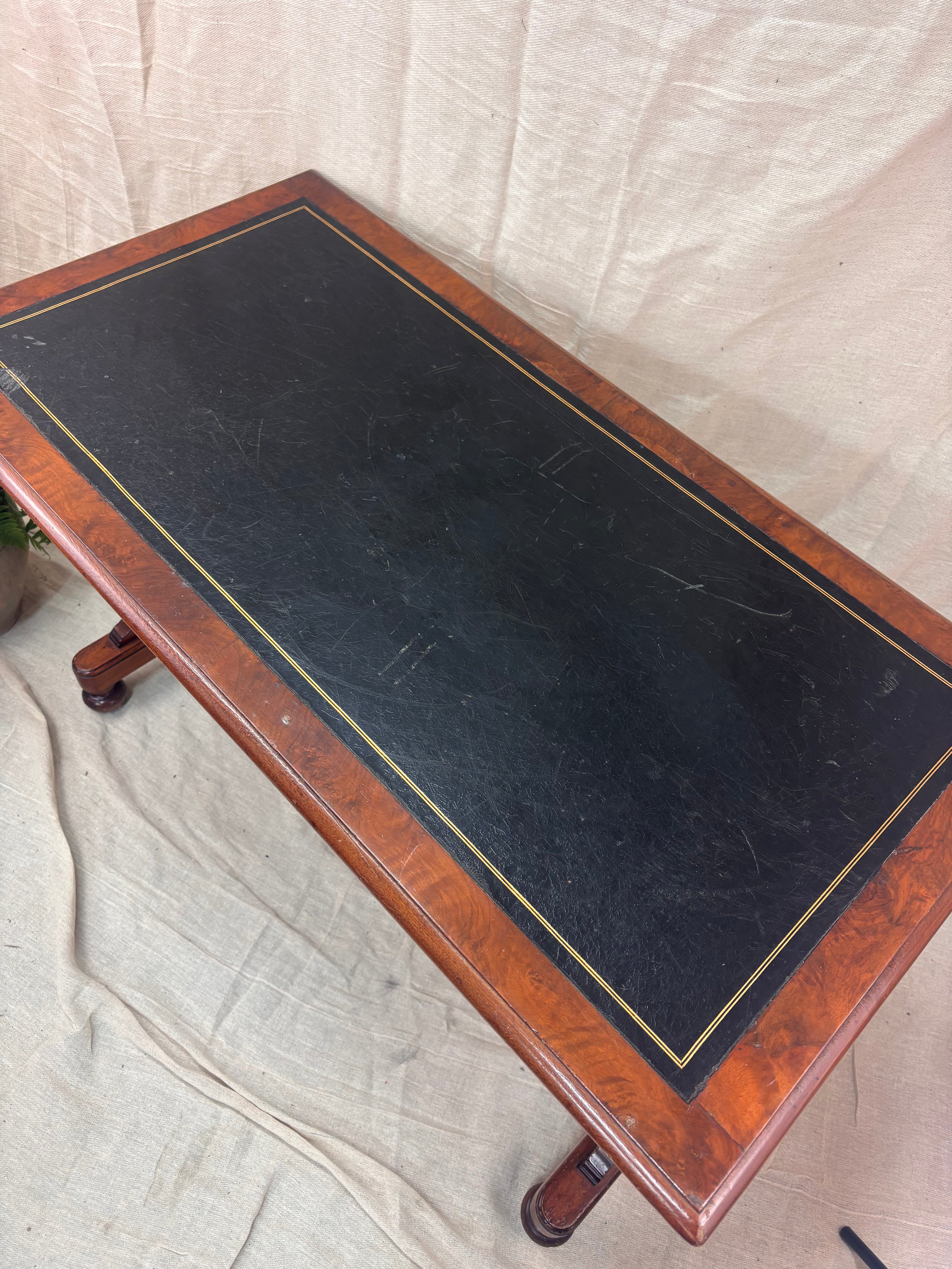 A small wooden table with a leather top against a cream background with a potted plant