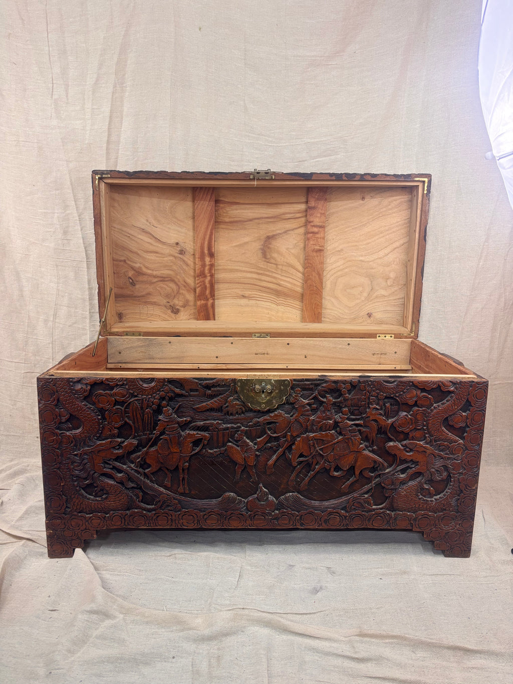 A carved wooden chest with the lid open on a cream background