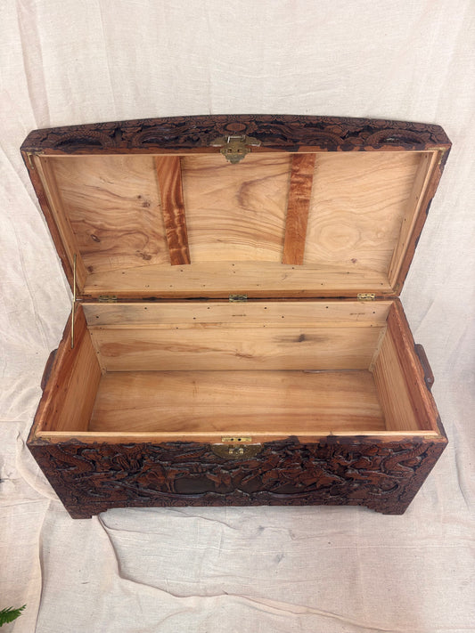 A carved wooden chest with the lid open showing an empty interior 