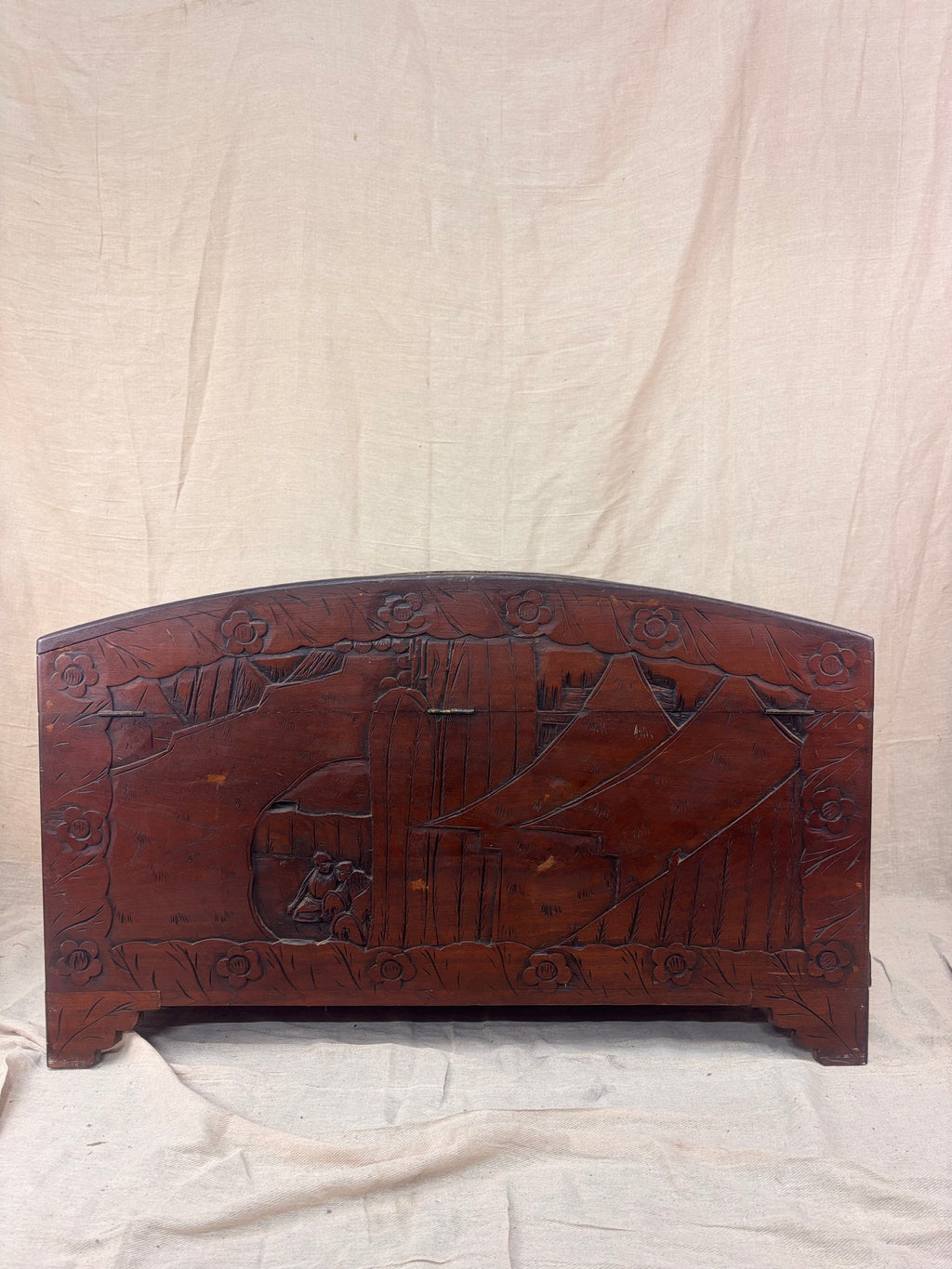 Back of a carved wooden chest with a curved lid and mountain scene