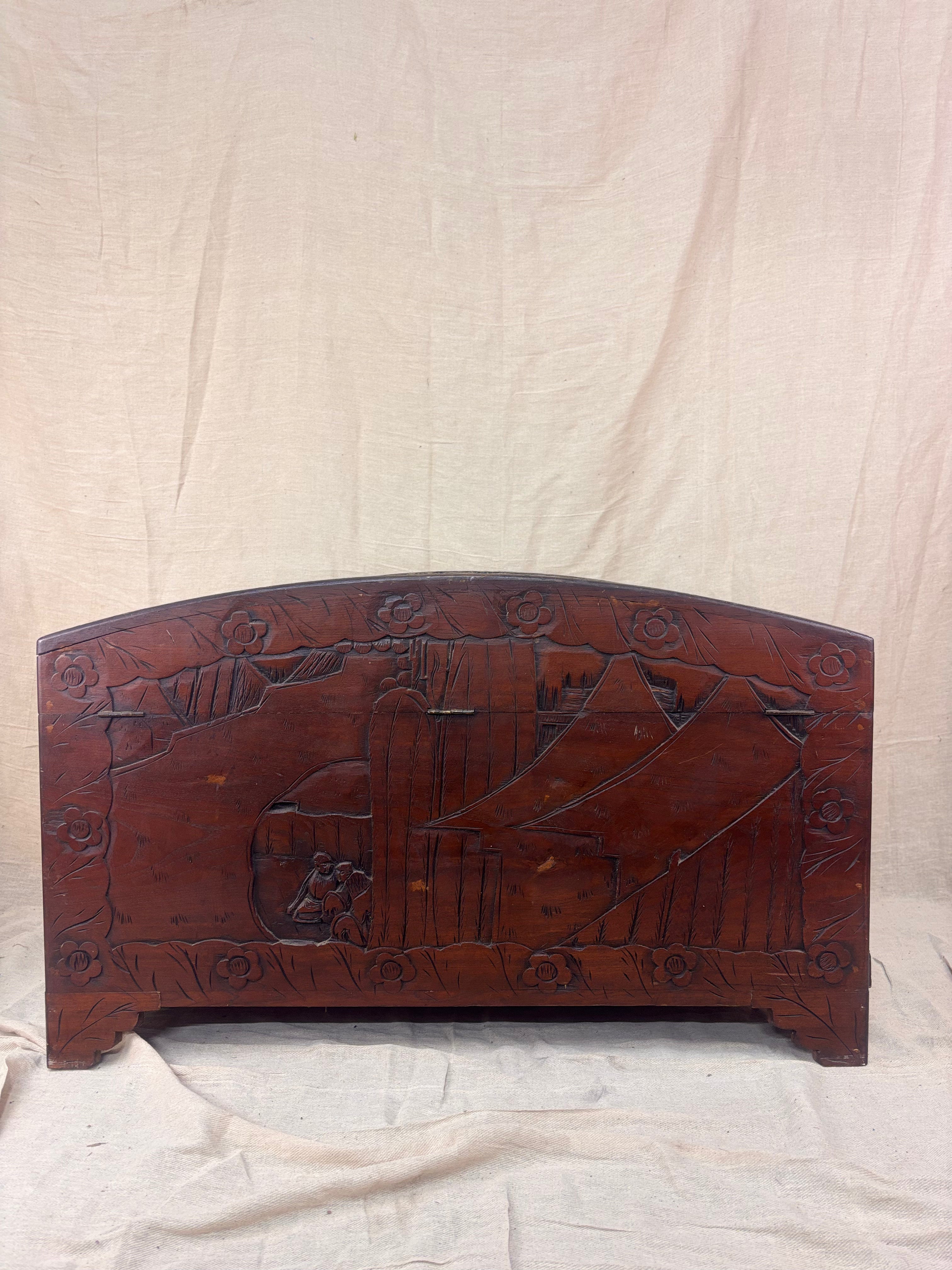 Back of a carved wooden chest with a curved lid and mountain scene