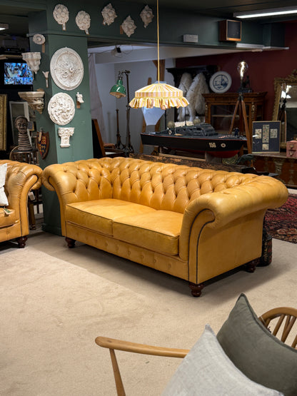 mustard leather sofa in a room with decorative items on the walls and floor.