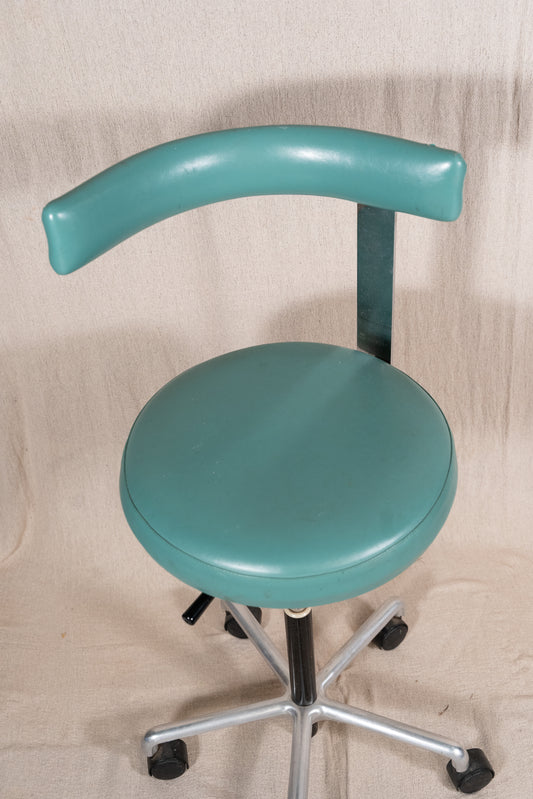 A teal-green swivel stool with a curved backrest, upholstered seat, and a five-star chrome base with black casters, set against a beige fabric backdrop.