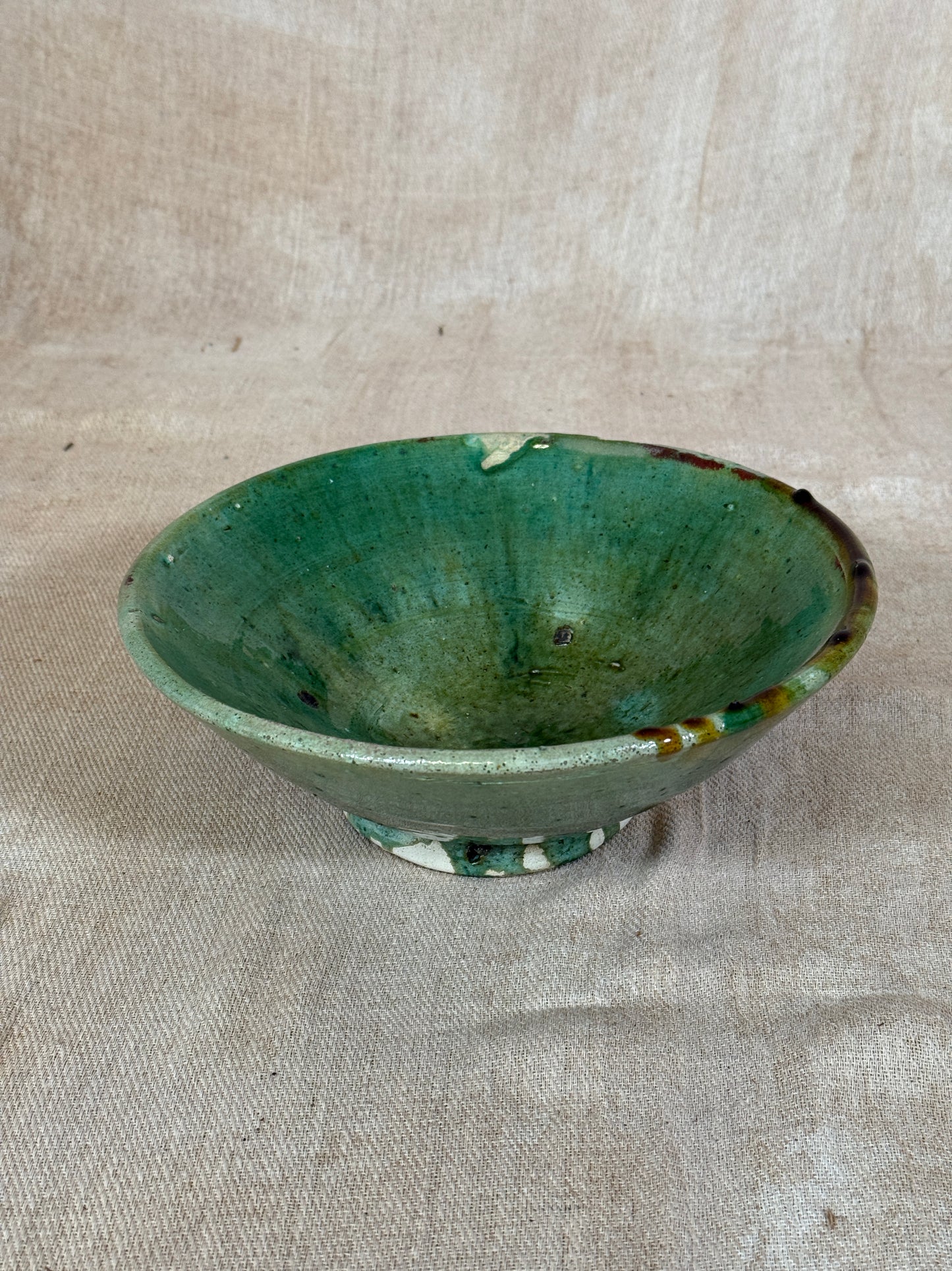 Green ceramic bowl on a beige fabric background