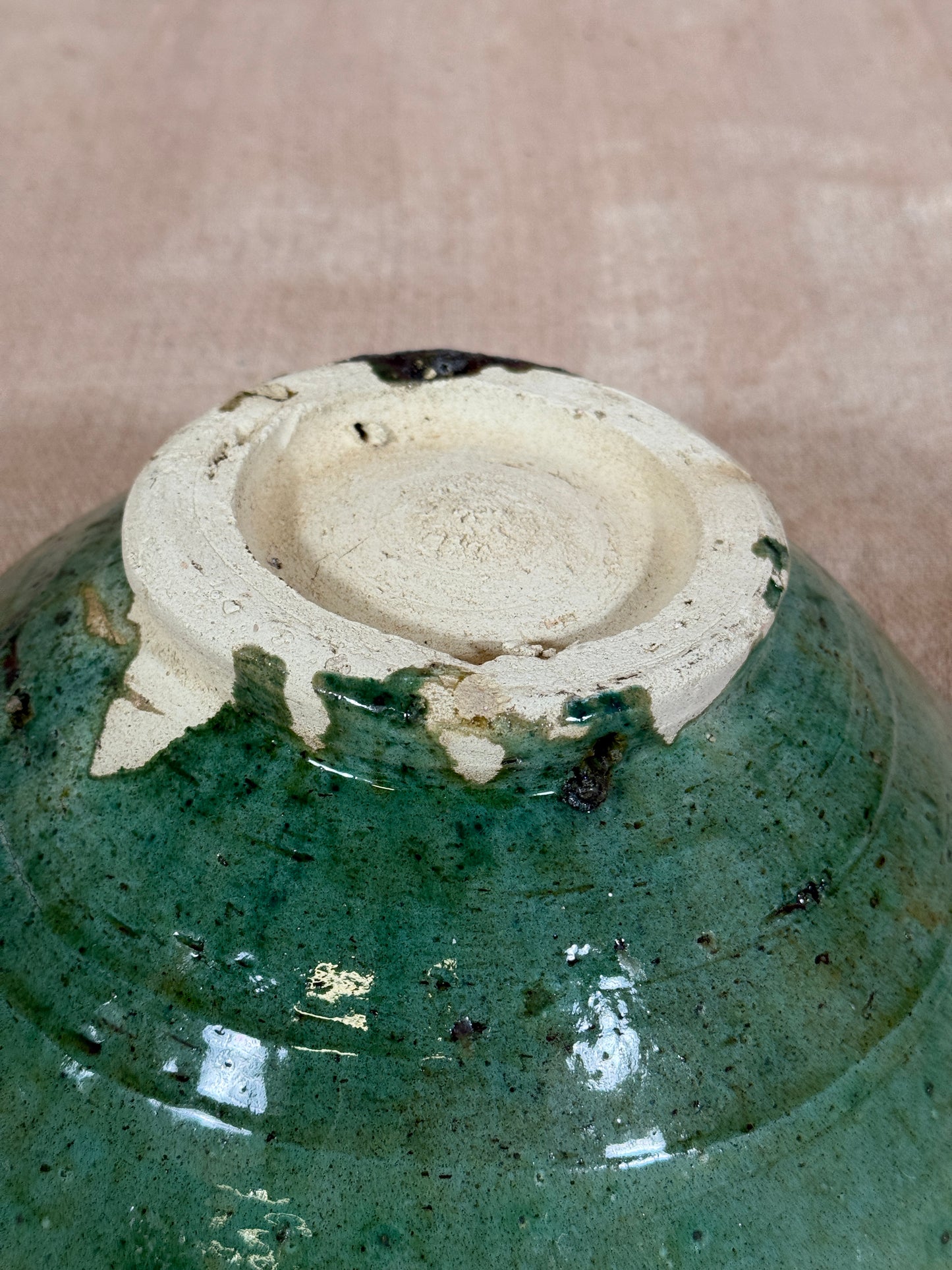 Close-up of a ceramic object with a green glaze and beige center on a brown background