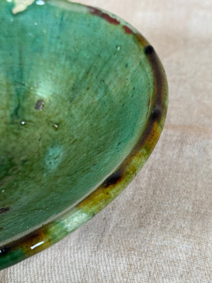 Close-up of a green ceramic bowl with a textured surface on a beige fabric background