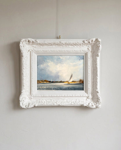 A framed landscape painting of sailboats on water, displayed in an ornate white frame hanging on a light gray wall.