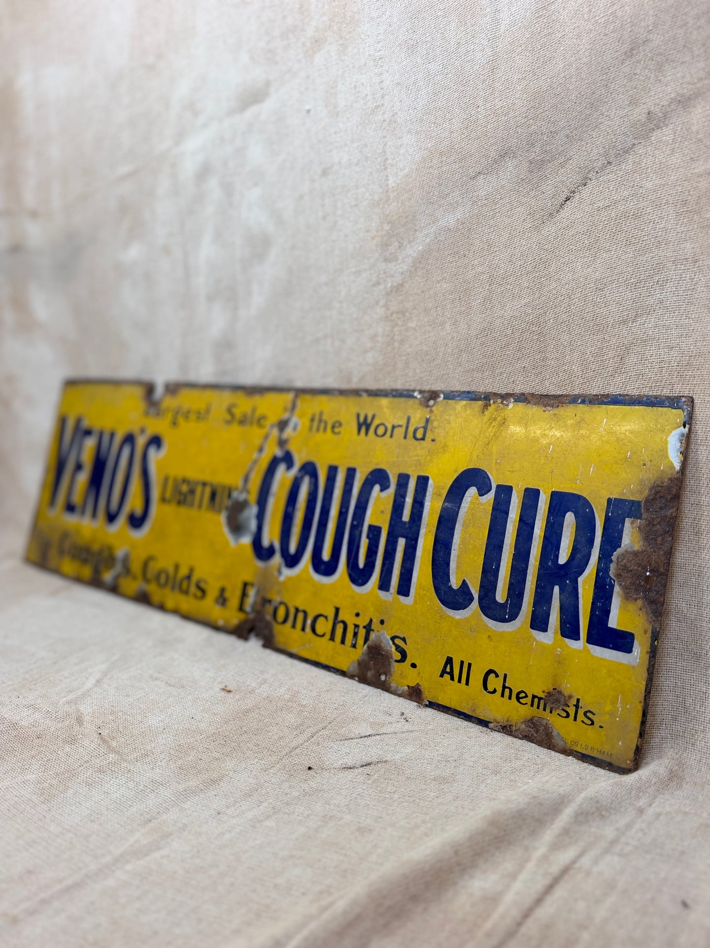 Vintage-style 'Cough Cure' sign with yellow background and blue text on a textured surface.
