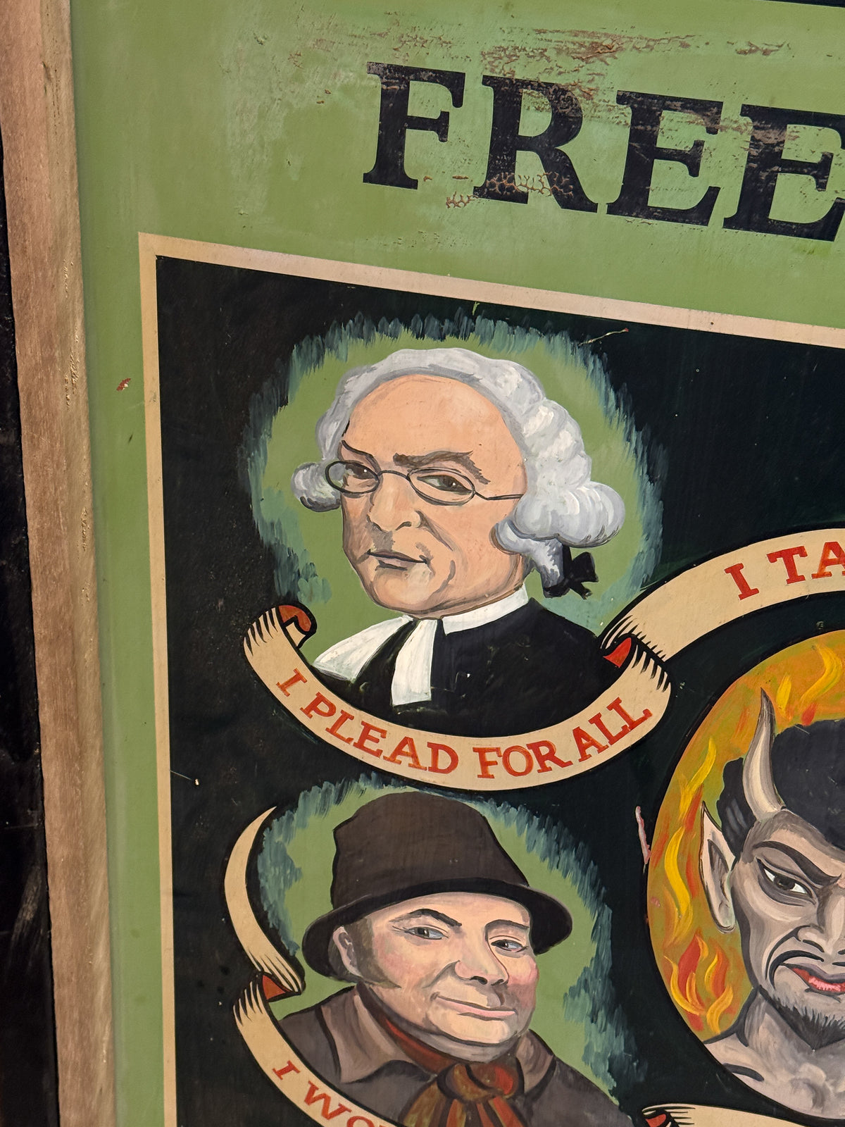 A close-up of a vintage painted poster or sign showing illustrated portraits with banners reading 'I PLEAD FOR ALL' and partial text 'FREE' at the top, mounted against a green background.