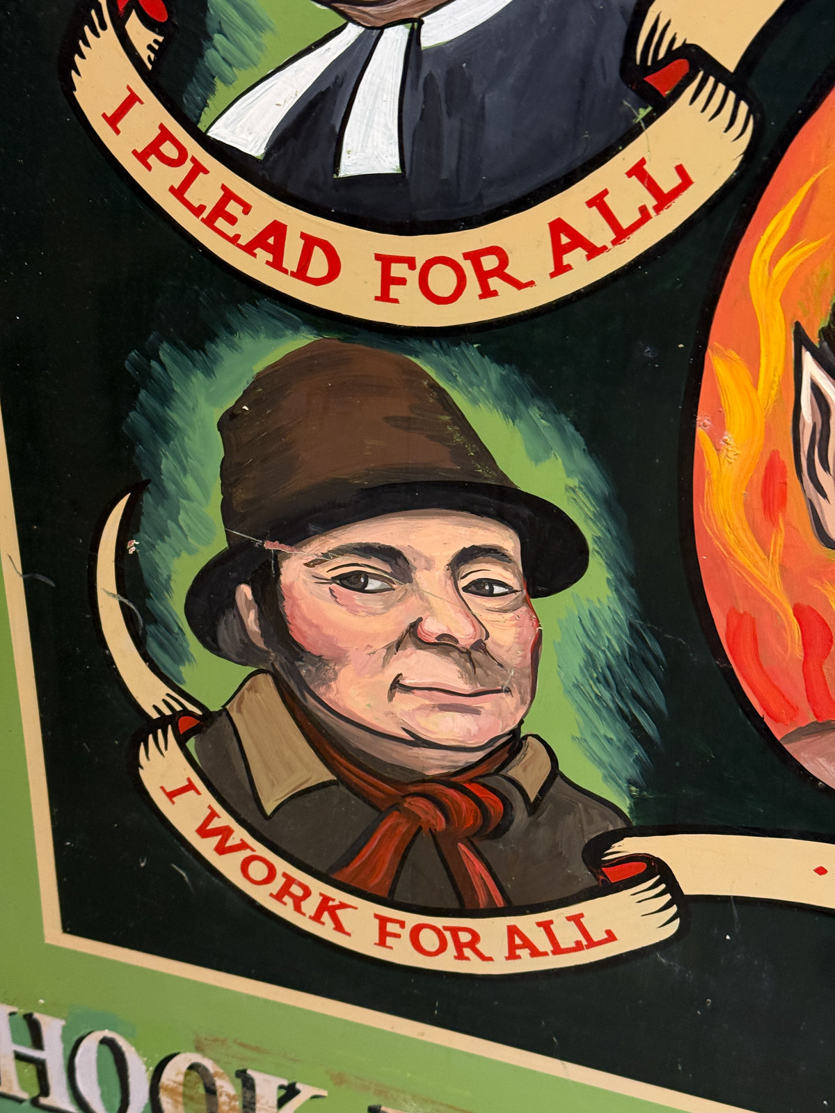 A close-up of a painted sign or poster featuring illustrated portraits with banners reading 'I PLEAD FOR ALL' and 'I WORK FOR ALL' on a dark background.