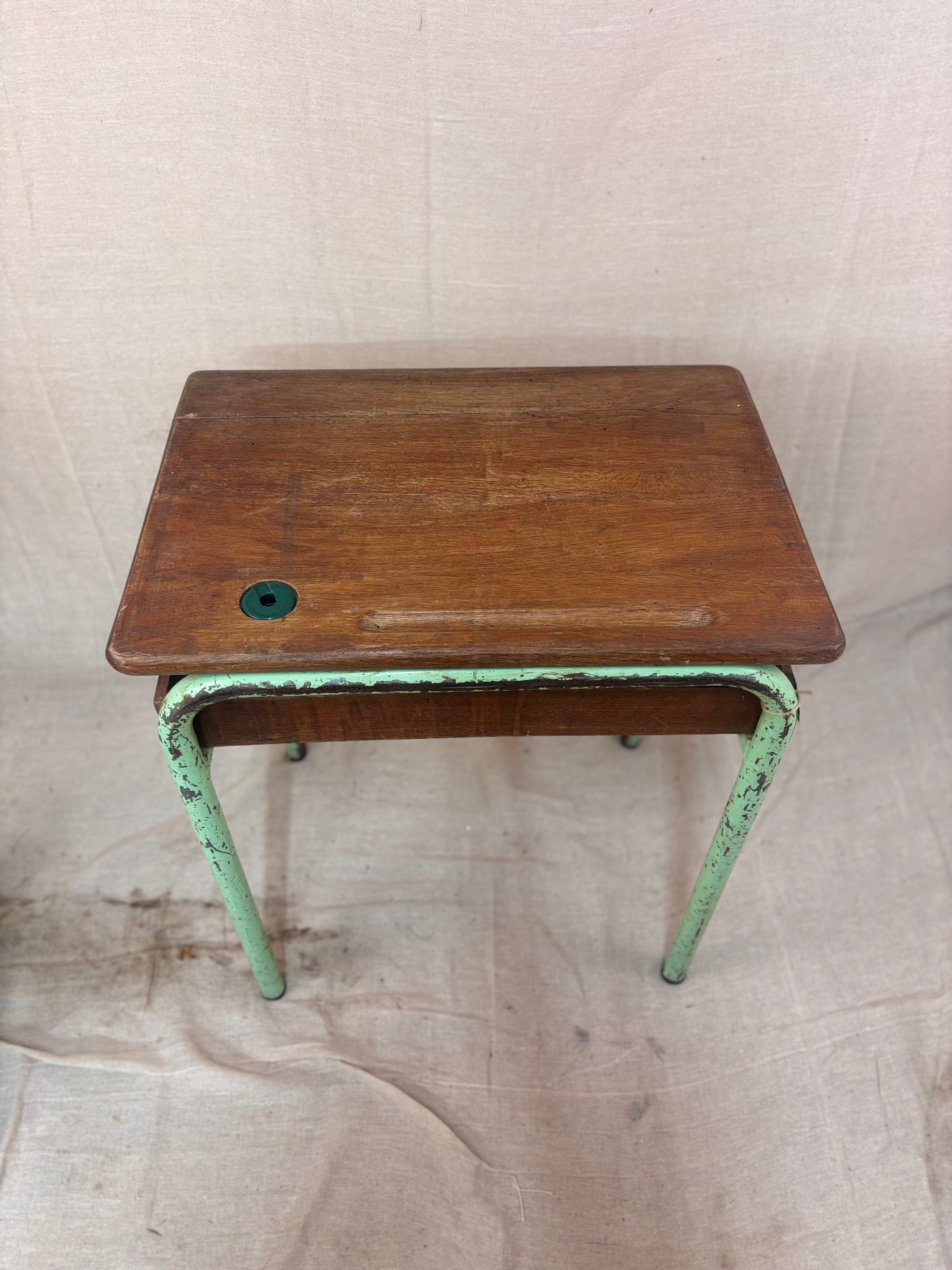 Vintage child’s school desk with a wooden top and green-painted metal frame, photographed against a cream backdrop.