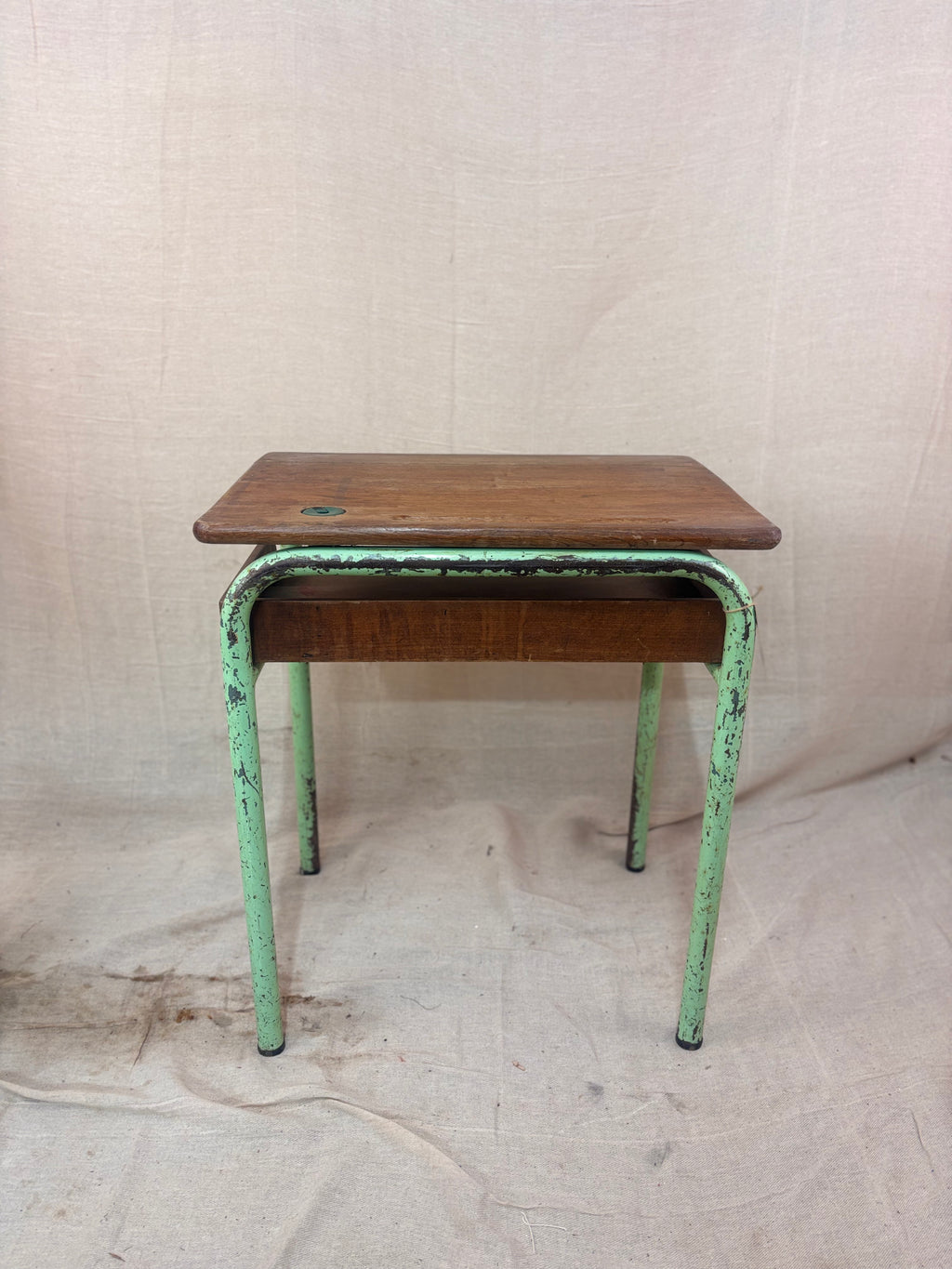 Vintage child’s school desk with a wooden top and green-painted metal frame, photographed against a cream backdrop.