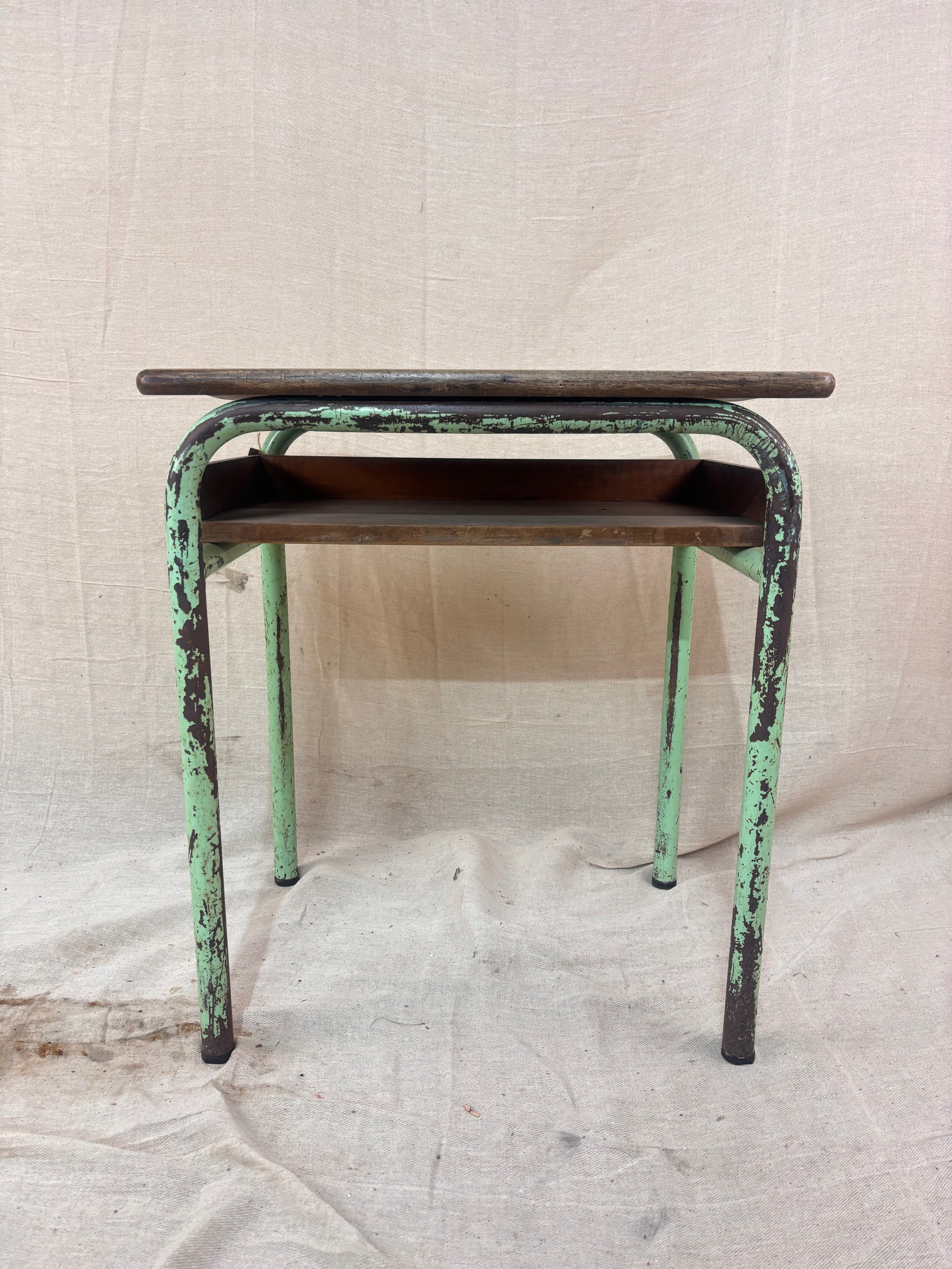 Vintage child’s school desk with a wooden top and green-painted metal frame, photographed against a cream backdrop.