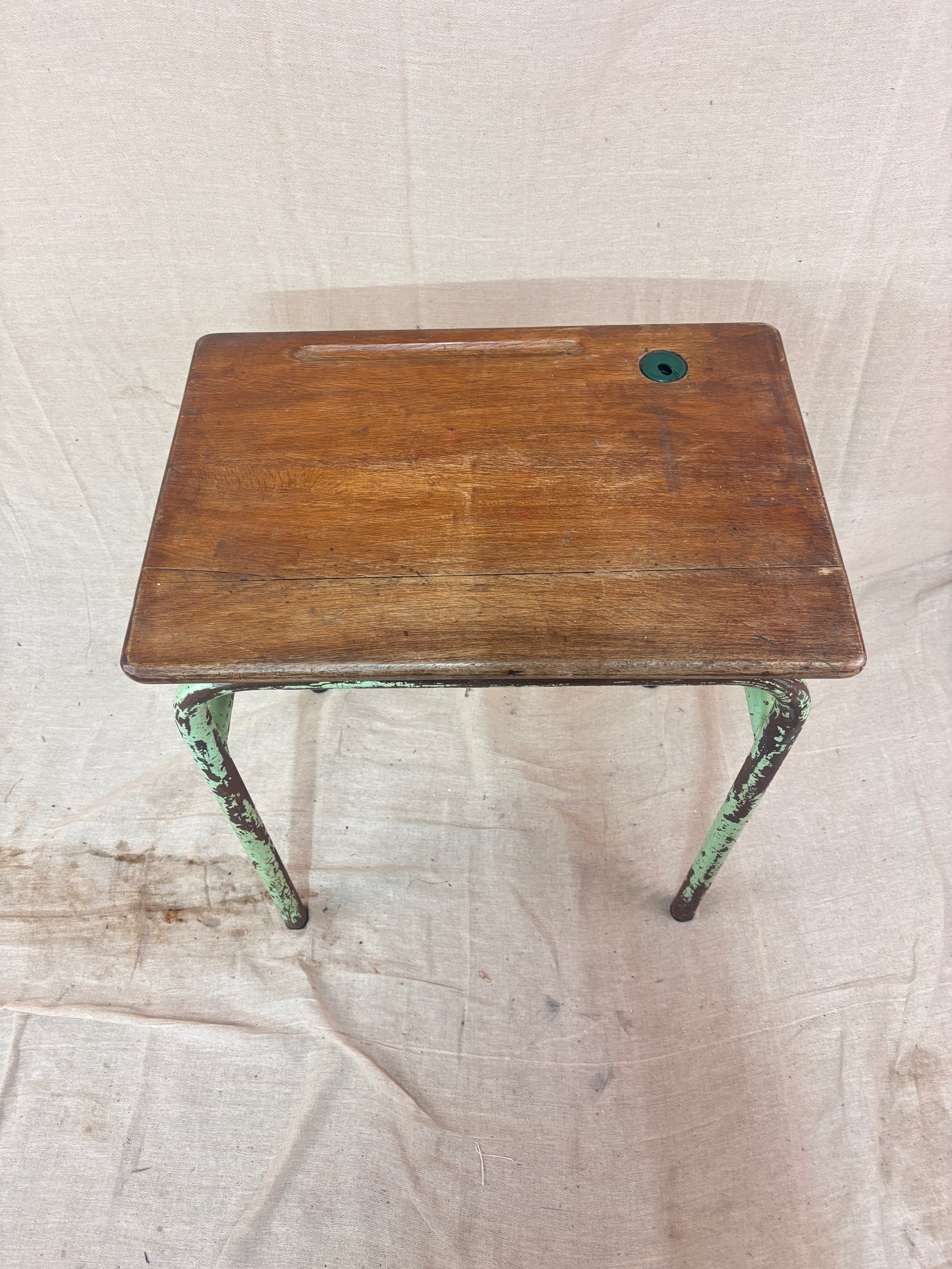 Vintage child’s school desk with a wooden top and green-painted metal frame, photographed against a cream backdrop.