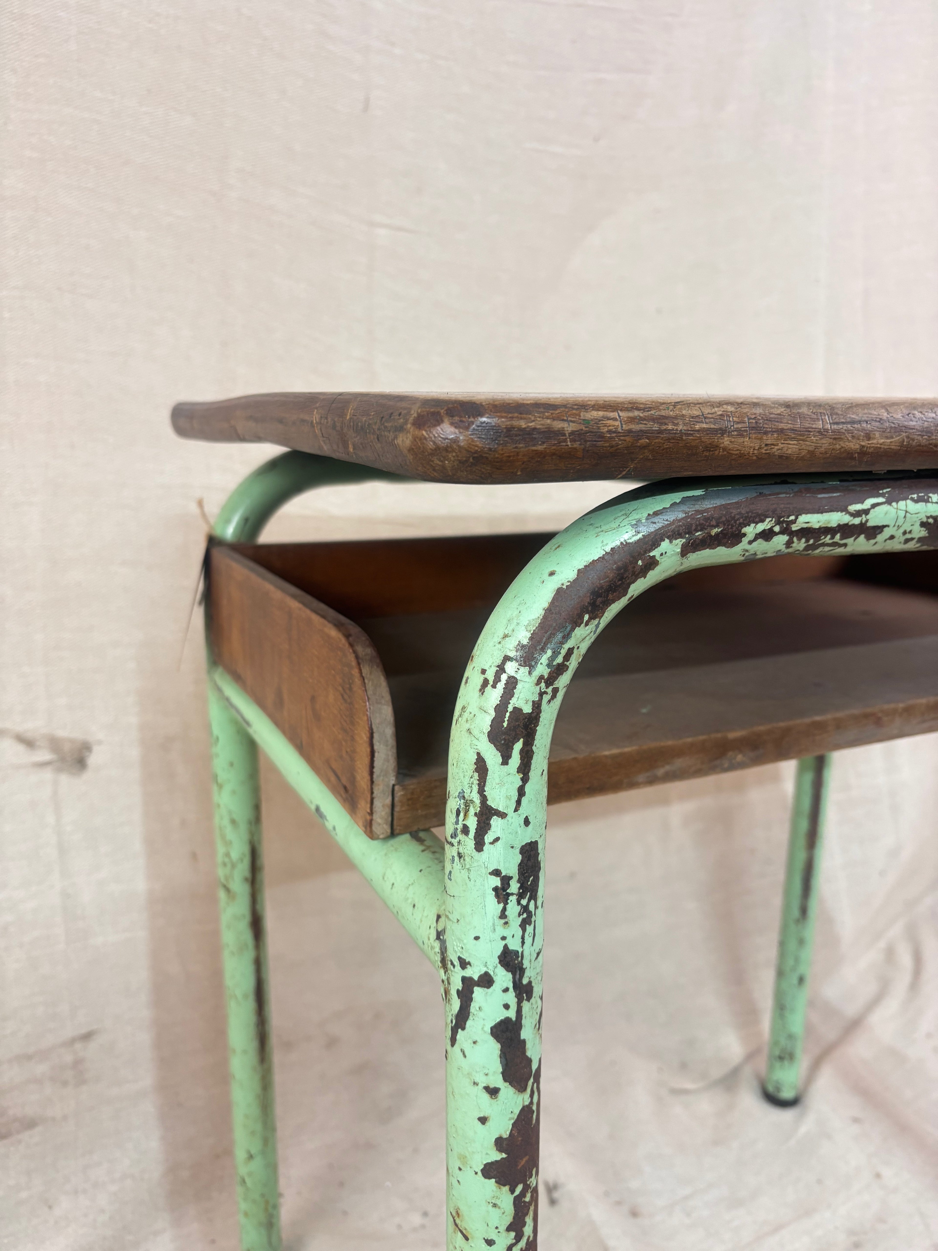 Vintage child’s school desk with a wooden top and green-painted metal frame, photographed against a cream backdrop.