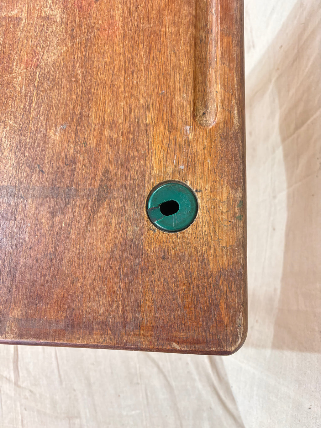 Vintage child’s school desk with a wooden top and green-painted metal frame, photographed against a cream backdrop.