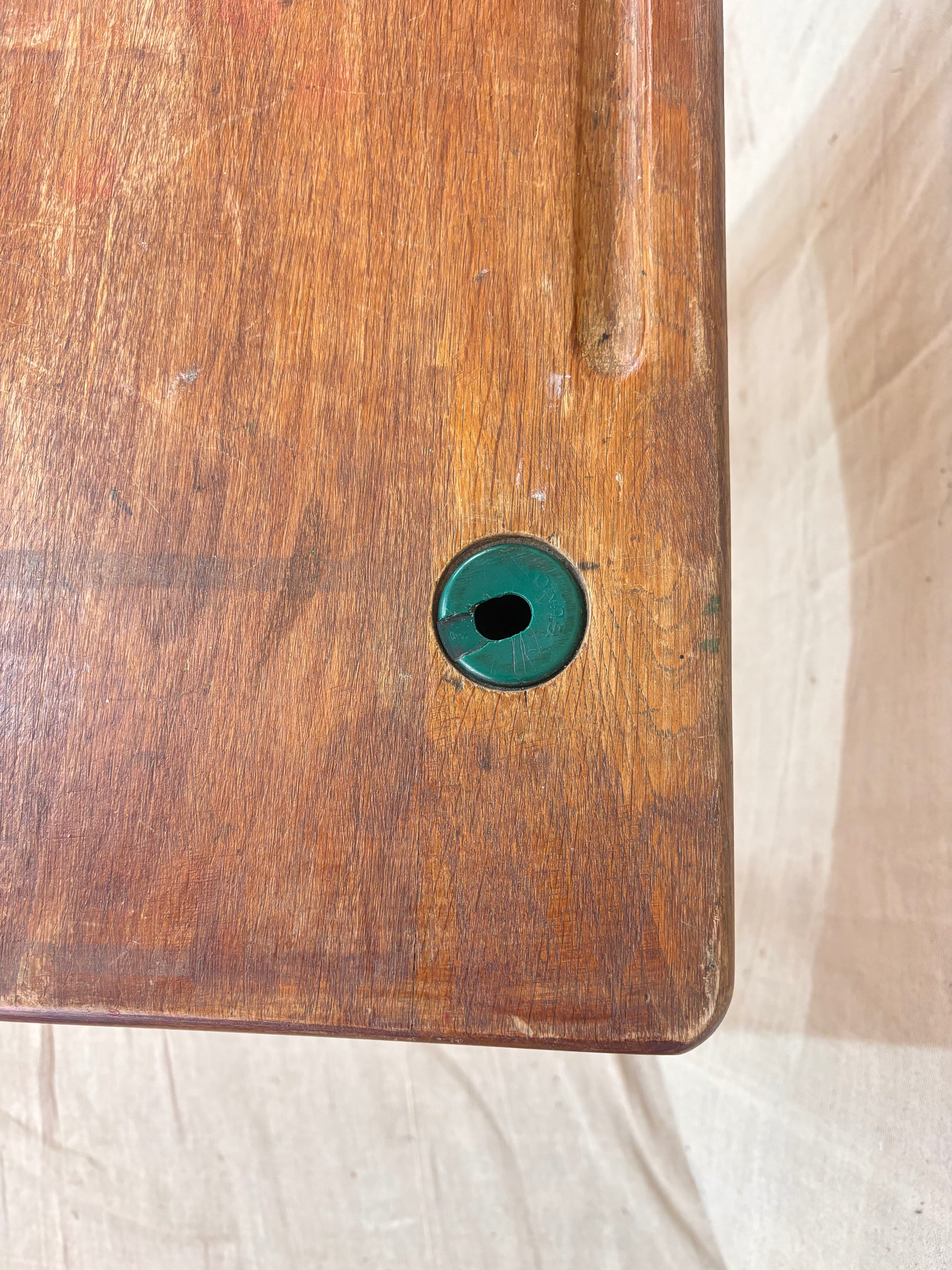 Vintage child’s school desk with a wooden top and green-painted metal frame, photographed against a cream backdrop.