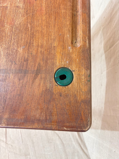 Vintage child’s school desk with a wooden top and green-painted metal frame, photographed against a cream backdrop.
