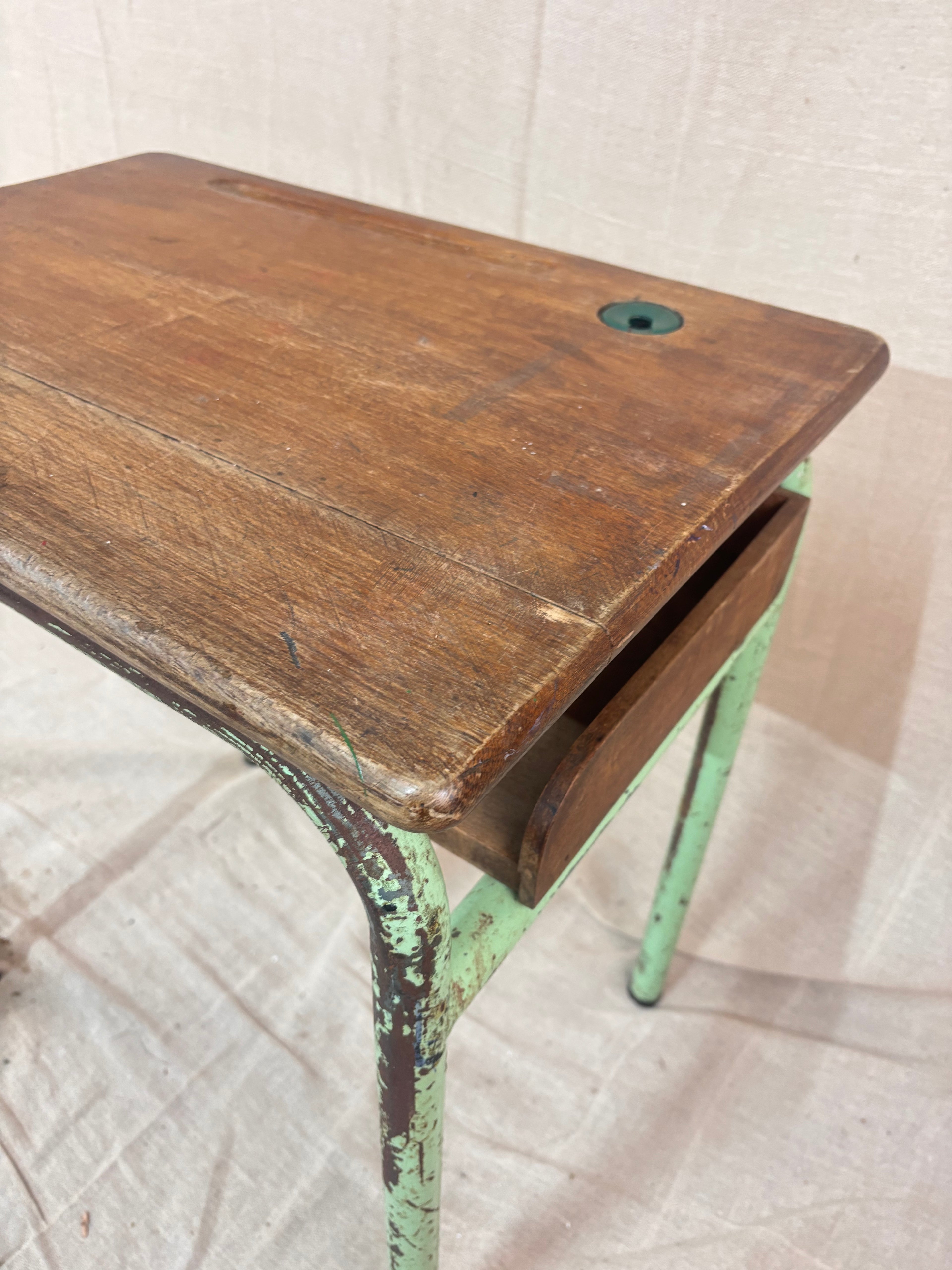 Vintage child’s school desk with a wooden top and green-painted metal frame, photographed against a cream backdrop.