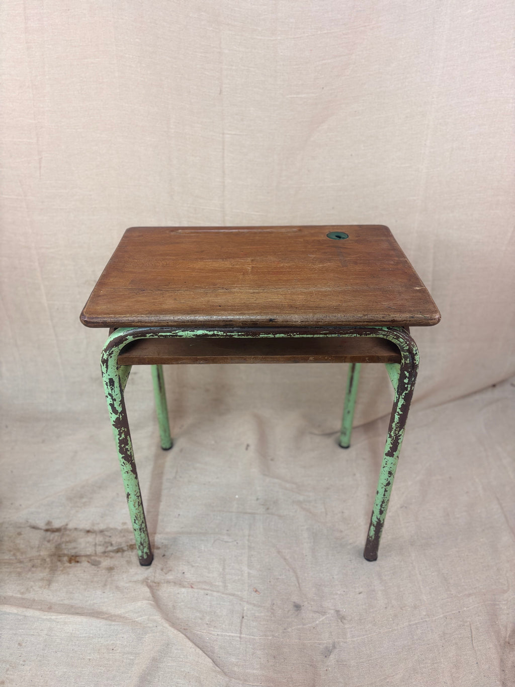 Vintage child’s school desk with a wooden top and green-painted metal frame, photographed against a cream backdrop.